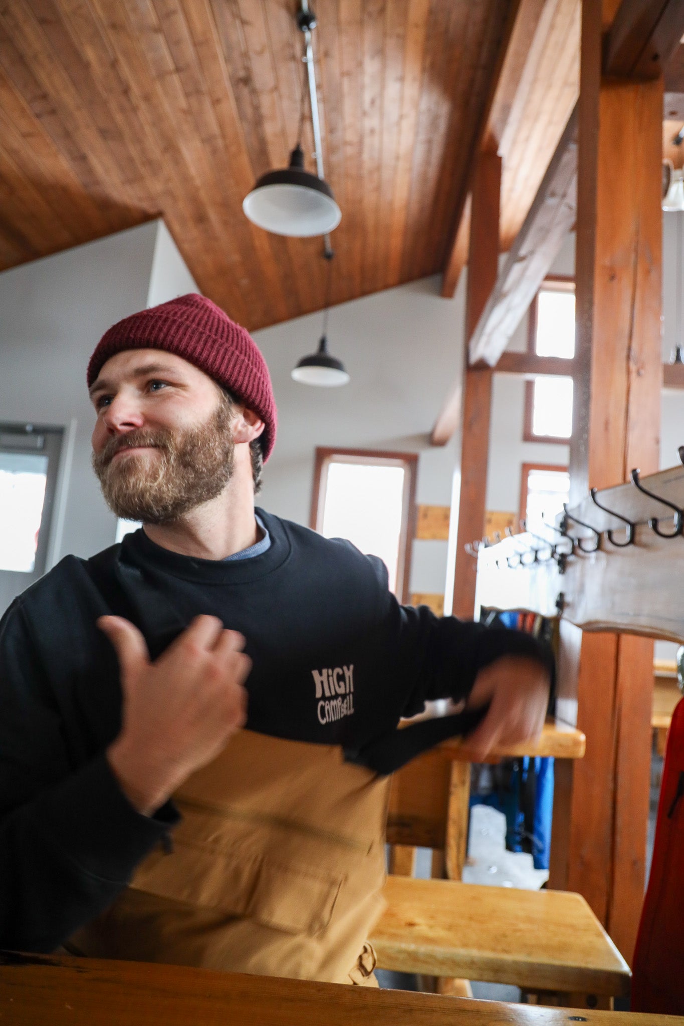 Man wearing a black sweatshirt with visible HIGH CAMPBELL in a wooden interior setting