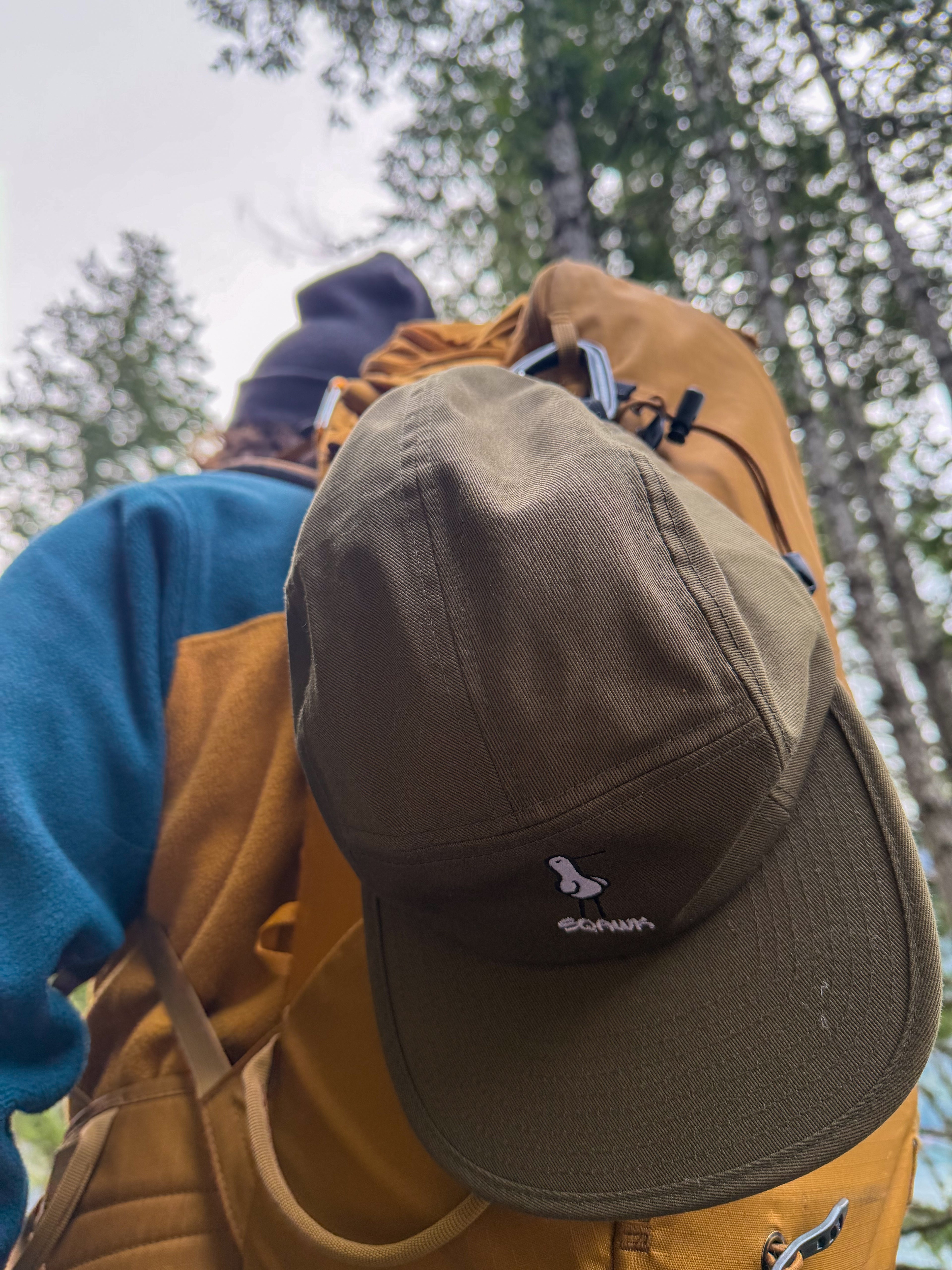 olive green 5 panel sqawk hat with seagull and sqawk lettering clipped to hiking backpack
