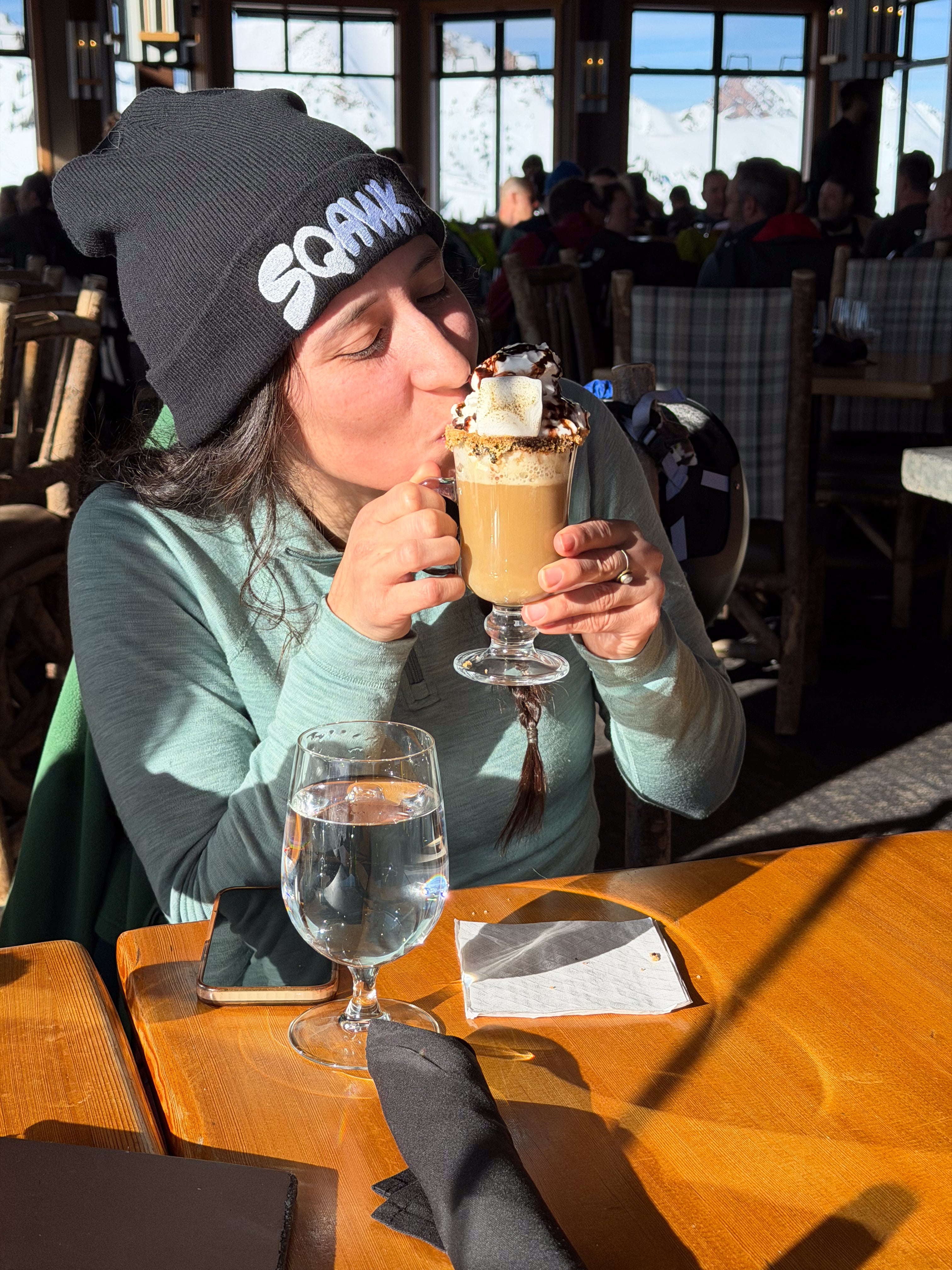 Woman drinking hot chocolate wearing a black SQAWK beanie